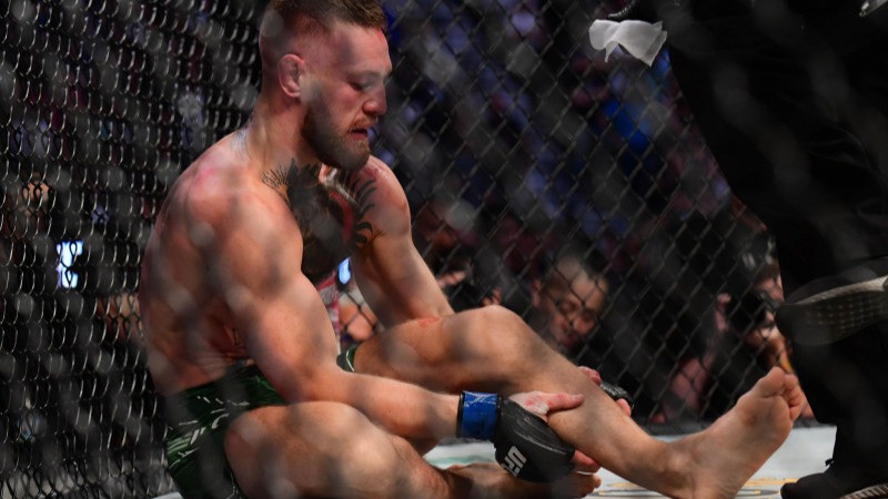 Petarung Conor McGregor memegang kakinya yang patah saat kalah dari Dustin Poirier di T-Mobile Arena di Las Vegas, Minggu WIB (11/7/2021)