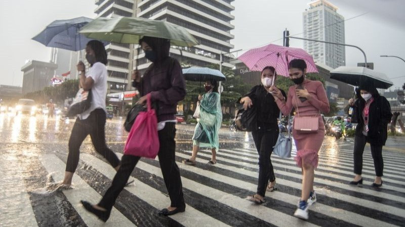 Warga berjalan menggunakan payung saat hujan turun di kawasan Sarinah Thamrin, Jakarta, Selasa (5/4/2022).