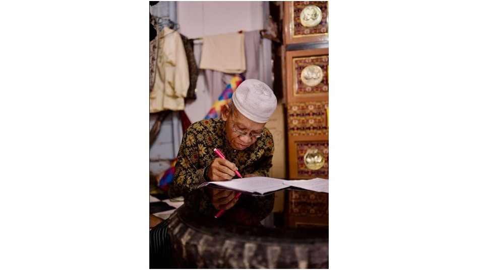 Wak Zuhdi, salah satu maestro seni Senandung Jolo, sedang menulis syair dan pantun untuk melatih generasi muda dalam Pelatihan Bersama Maestro.