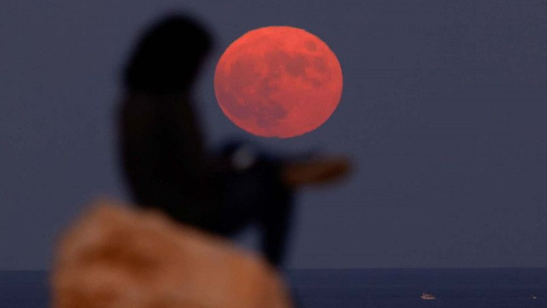 Seorang perempuan duduk di atas sebuah batu saat bulan purnama, yang dikenal sebagai Hunter s Moon, terlihat di I-Ahrax Point di Marfa Ridge, di luar desa Mellieha, Malta.