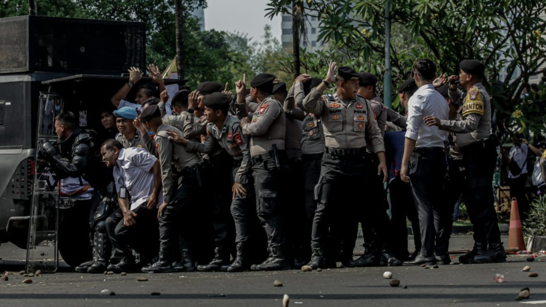 Aparat kepolisian berlindung dari lemparan batu yang dilayangkan massa penolak eksekusi Hotel Sultan.